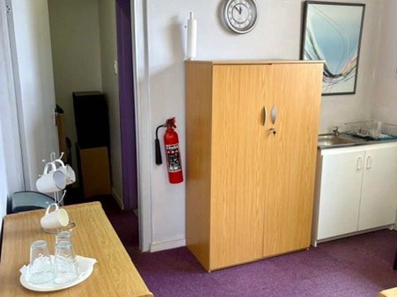 A functional utility space featuring a small kitchenette area with a sink, fire safety equipment, and carpeted flooring.