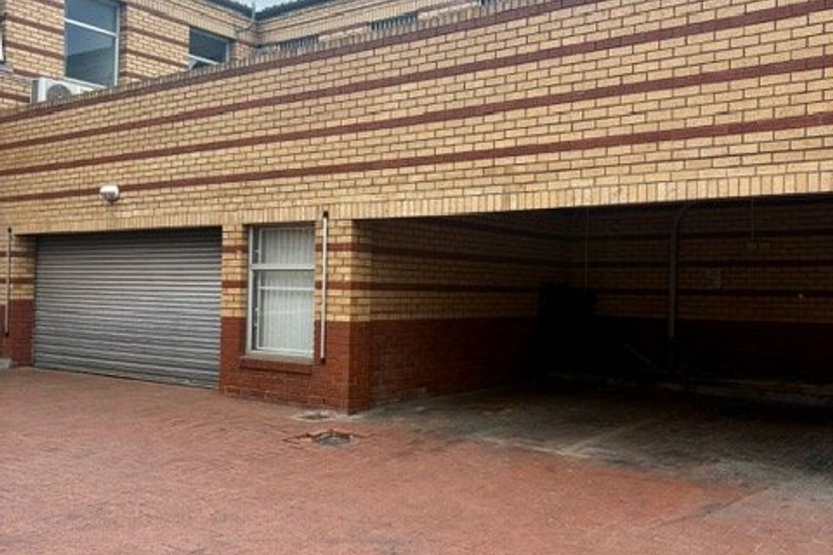 Rear exterior view of a commercial building featuring a paved driveway, covered parking area, and a secure roller shutter door.