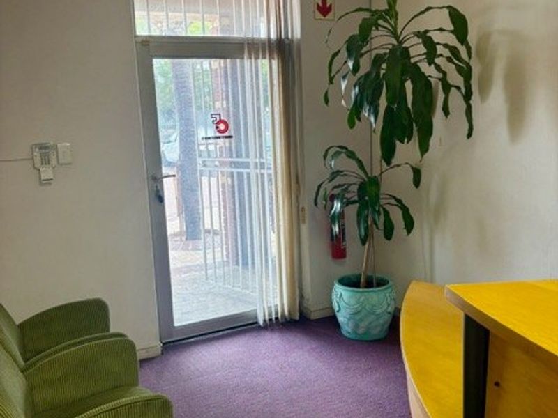 Commercial entrance area featuring a glass door with security gate, suspended ceiling, and carpeted flooring.