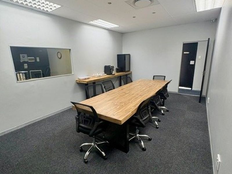 A functional office meeting room featuring carpeted flooring, recessed ceiling lighting, and a wall-mounted shelf.