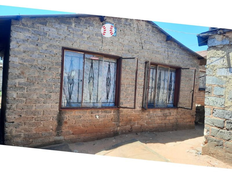 Rear exterior view of a brick house featuring security bars on the windows and visible signs of weathering on the masonry.
