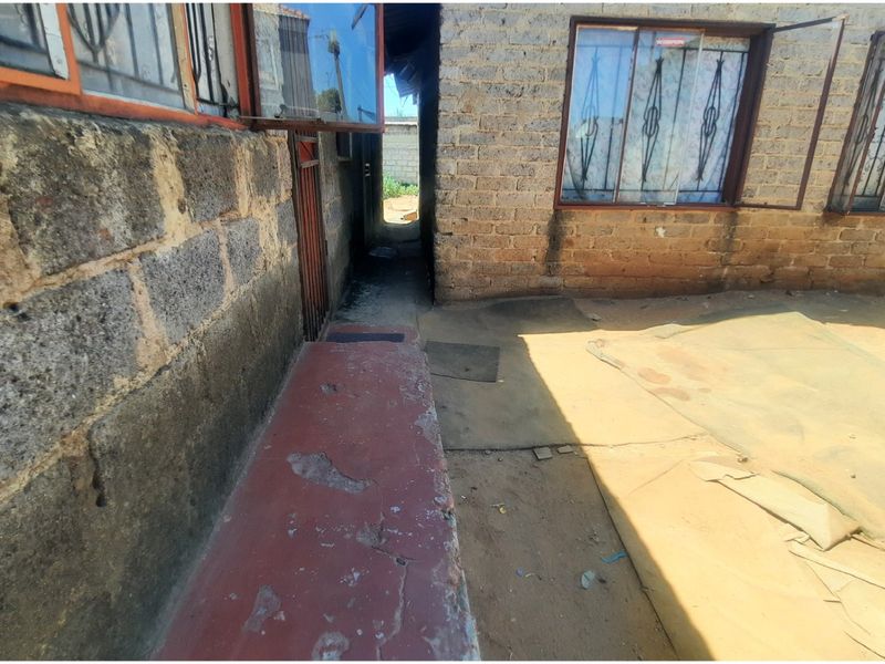 Exterior view of the rear of the property showing exposed brick walls, security bars on windows, and a weathered concrete pathway.