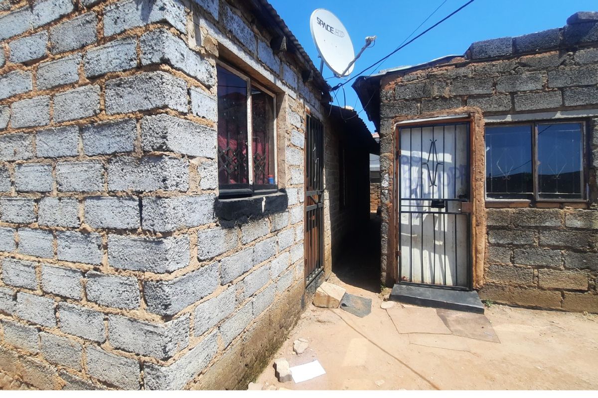 Exterior view of the rear of the property featuring concrete block construction, metal security gates, and aluminium window frames.