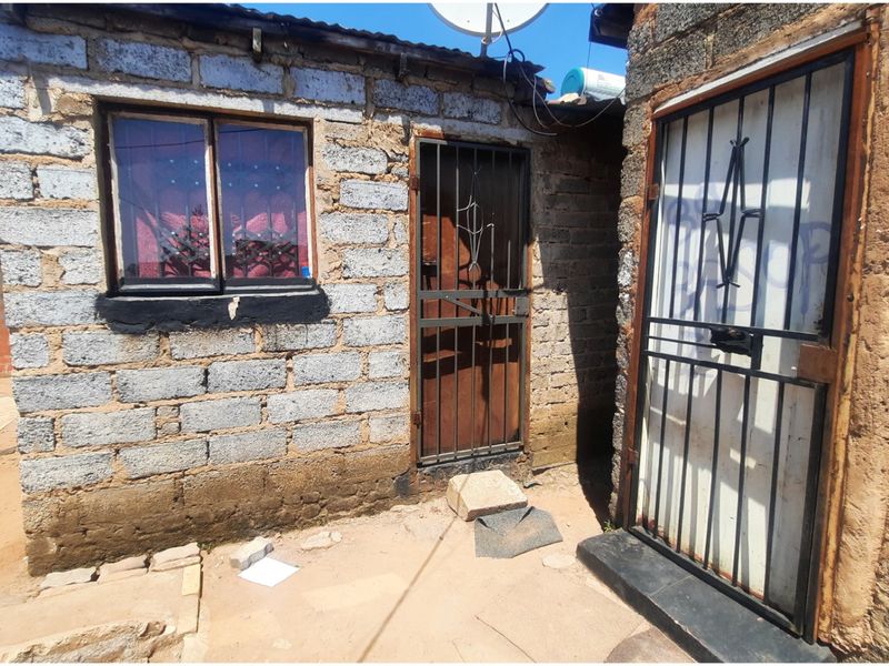 Exterior view of a residential structure featuring concrete block walls, security gates, and metal window frames.