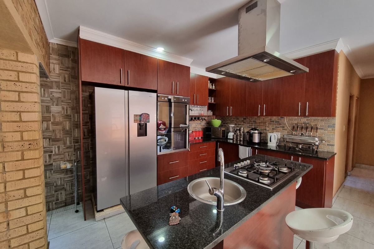 A well-appointed kitchen featuring dark wood cabinetry, granite countertops, a central island with a gas hob, and a modern stainless steel extractor fan.