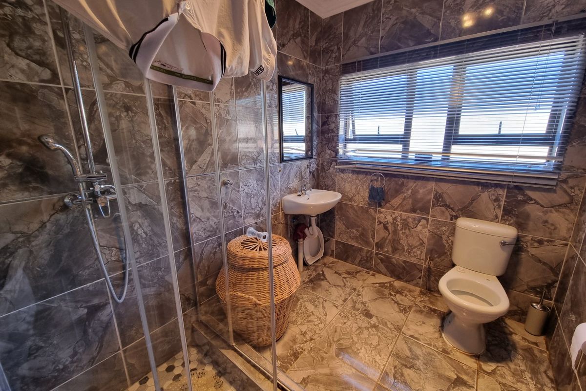 A tiled bathroom featuring a shower enclosure, wall-mounted basin, and toilet, finished with marble-effect wall and floor tiles.