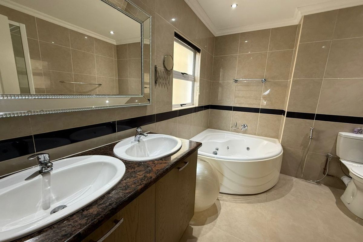 A well-appointed bathroom featuring a double vanity with granite countertop, a corner jetted bathtub, and full-height wall tiling.