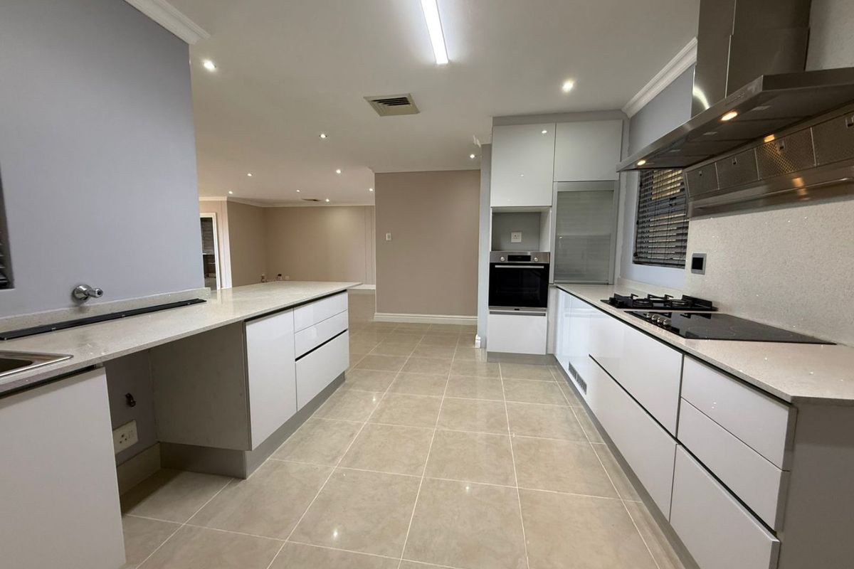 Modern kitchen featuring sleek white cabinetry, stone countertops, integrated oven, gas hob, and stainless steel extractor fan, flowing into an open-plan living area.