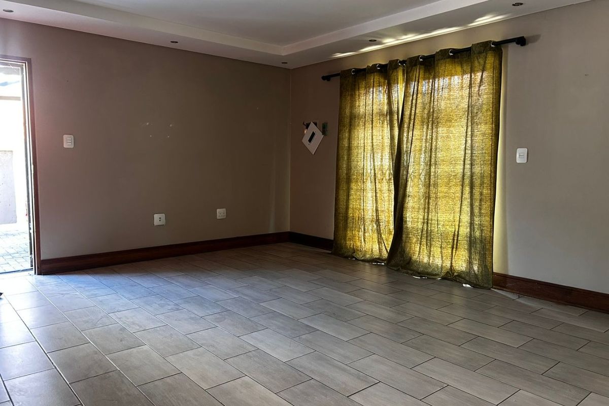 An empty living room featuring neutral tiled flooring, recessed ceiling lighting, and a sliding glass door providing access to the exterior.