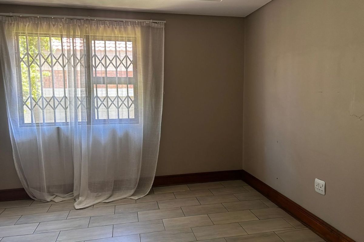 A vacant bedroom featuring neutral wall tones, tiled flooring, and a window fitted with a security gate.