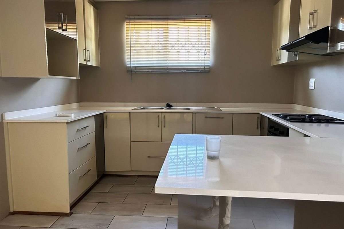 A clean, modern kitchen featuring high-gloss cabinetry, stone countertops, a gas hob with extractor fan, and neutral tiled flooring.