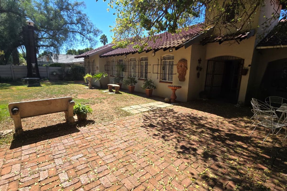 A rear exterior view featuring a brick-paved patio area, a landscaped garden, and a house with a tiled roof and security-fitted windows.