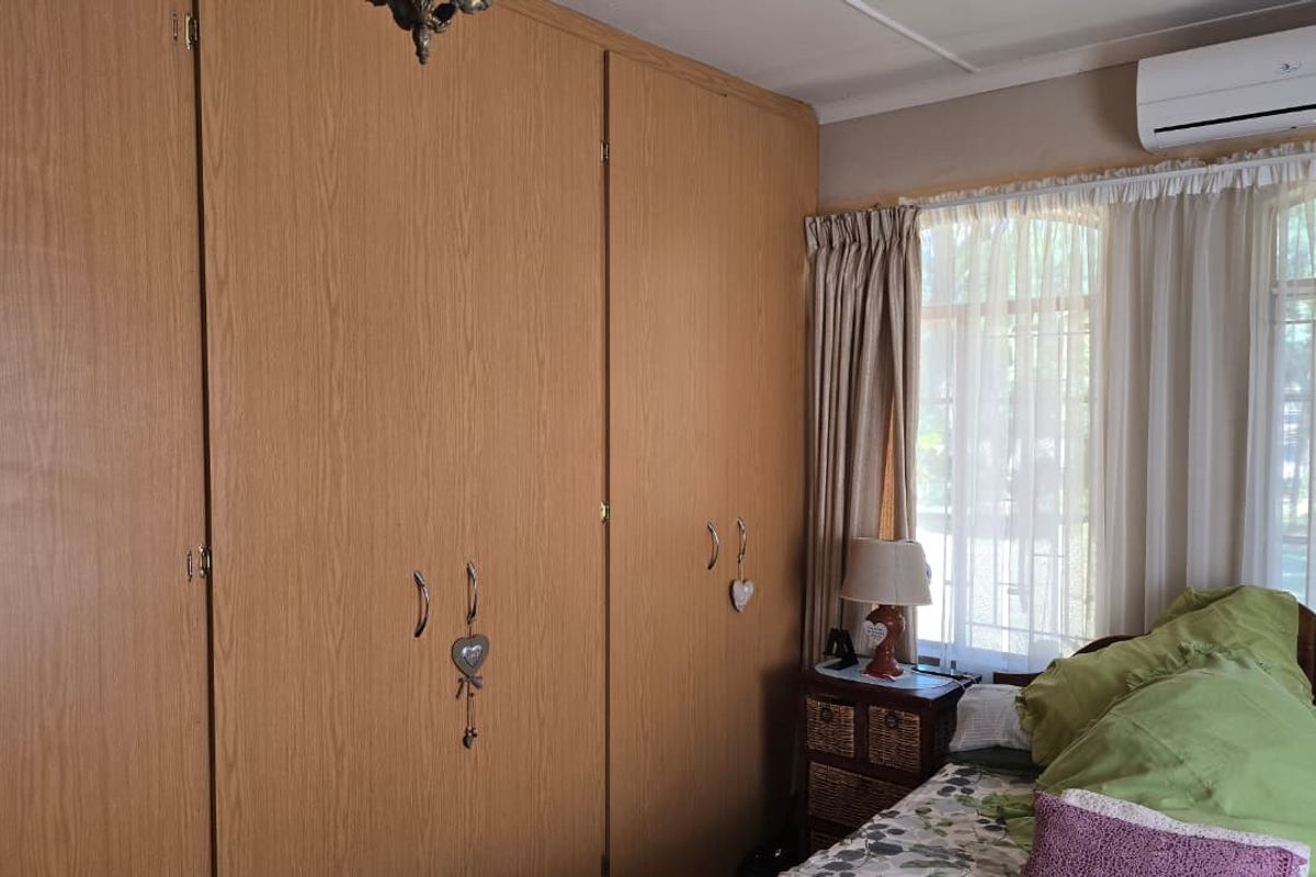 A bedroom featuring floor-to-ceiling built-in wooden cupboards and a wall-mounted split-system air conditioning unit.