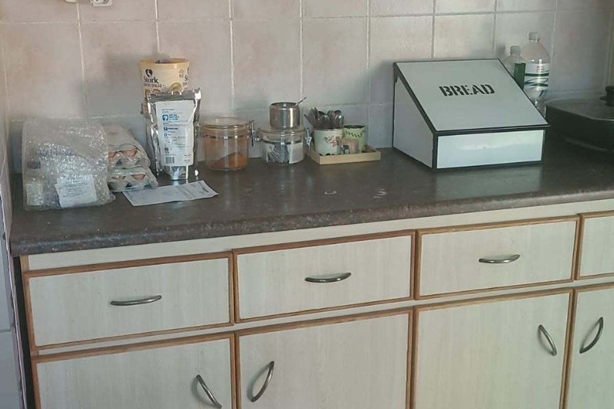 A functional kitchen area featuring light-toned laminate cabinetry, tiled splashbacks, and durable floor tiles, offering a practical workspace with ample storage.