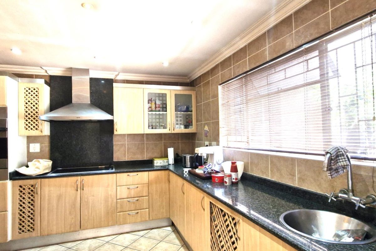 A functional kitchen featuring wooden cabinetry, granite countertops, a built-in oven, extractor fan, and tiled backsplash with a large window for natural light.