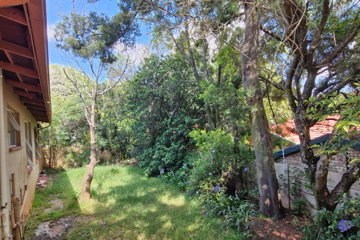 A view of the rear garden area featuring mature trees, lawn, and a concrete boundary wall adjacent to the house exterior.