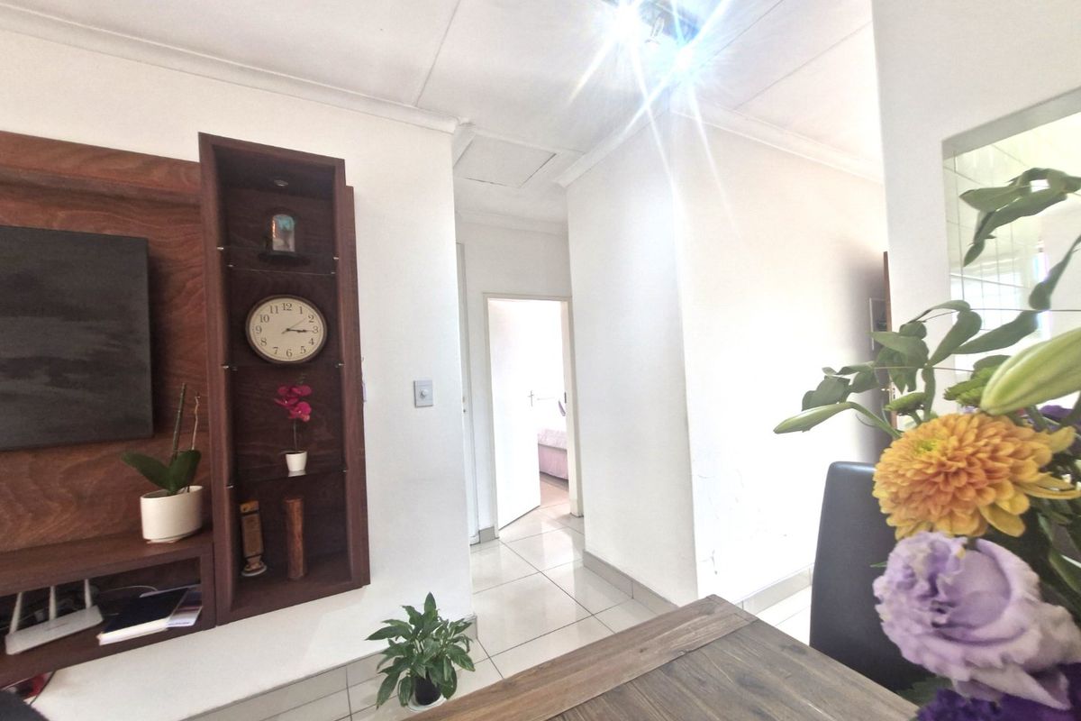 A living area featuring a built-in wooden shelving unit and tiled flooring, leading into a hallway with access to an adjacent bedroom.