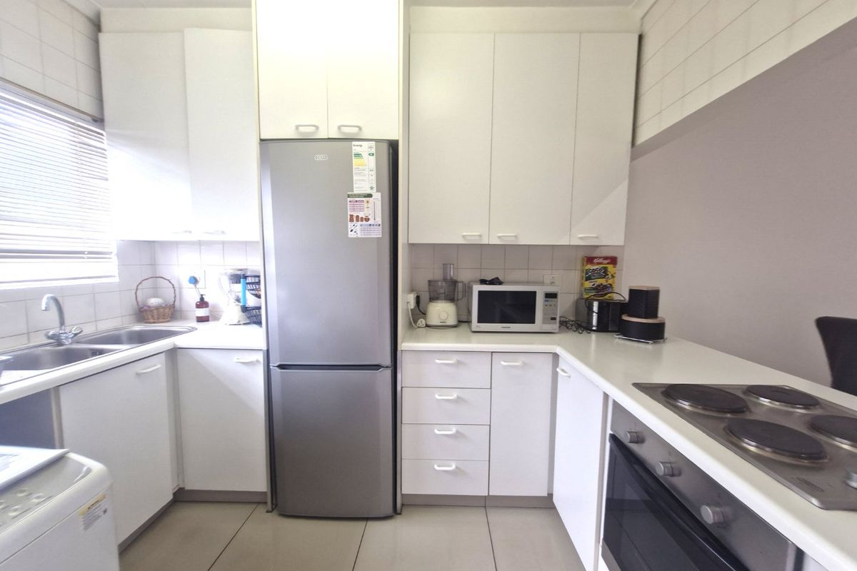 A functional kitchen featuring white cabinetry, tiled splashbacks, a stainless steel sink, and integrated electric cooking appliances.