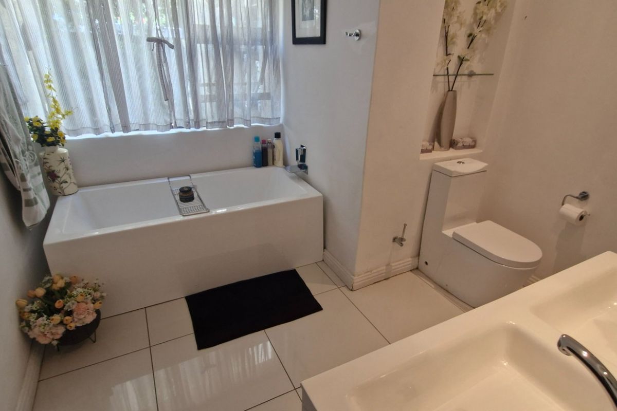 A clean, modern bathroom featuring a built-in bathtub, a dual vanity sink, and a toilet with tiled flooring and a recessed wall niche.