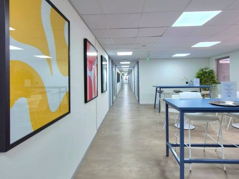 A bright commercial hallway featuring a suspended acoustic tile ceiling, recessed lighting, and durable vinyl flooring, providing access to multiple office spaces.