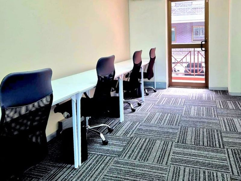 A functional office space featuring carpeted flooring, a wall-mounted air conditioning unit, and a glass-paneled door providing natural light and exterior access.