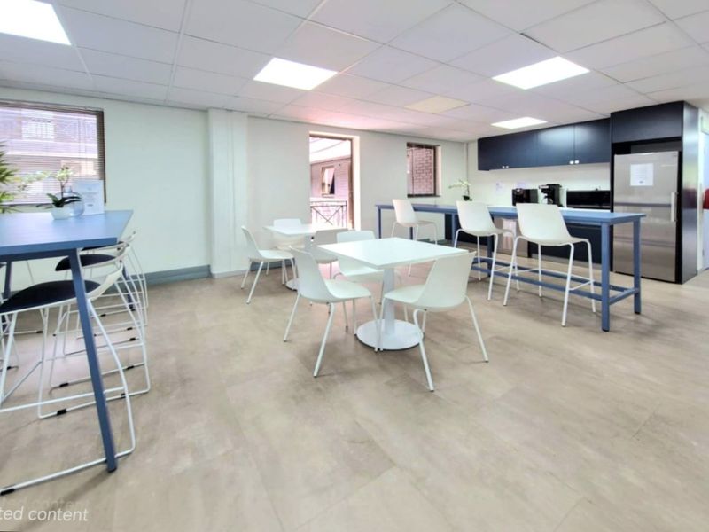 A modern commercial breakroom or kitchenette area featuring built-in dark cabinetry, integrated appliances, and a functional layout with durable flooring and recessed ceiling lighting.
