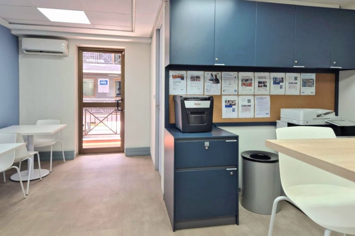 A functional commercial office space featuring built-in blue cabinetry, a cork notice board, recessed ceiling lighting, and a wall-mounted air conditioning unit.