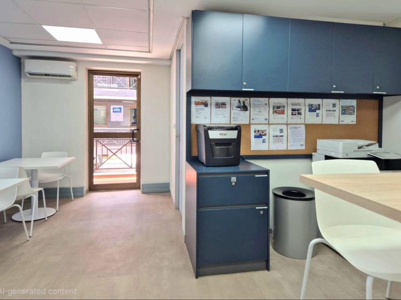 A functional commercial office space featuring built-in blue cabinetry, a cork notice board, recessed ceiling lighting, and a wall-mounted air conditioning unit.