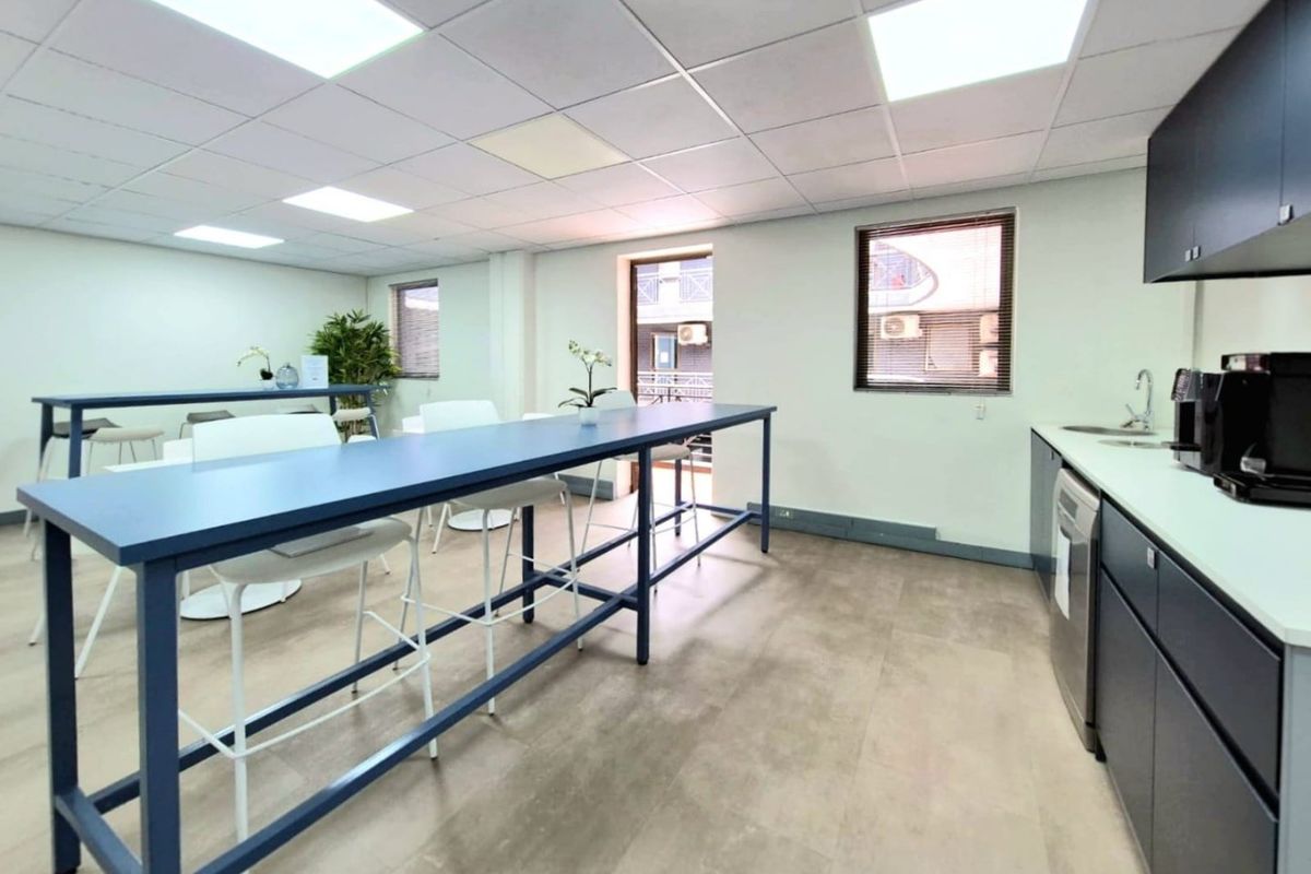 Modern commercial kitchenette and break area featuring sleek dark cabinetry, integrated sink, and durable flooring with recessed ceiling lighting.