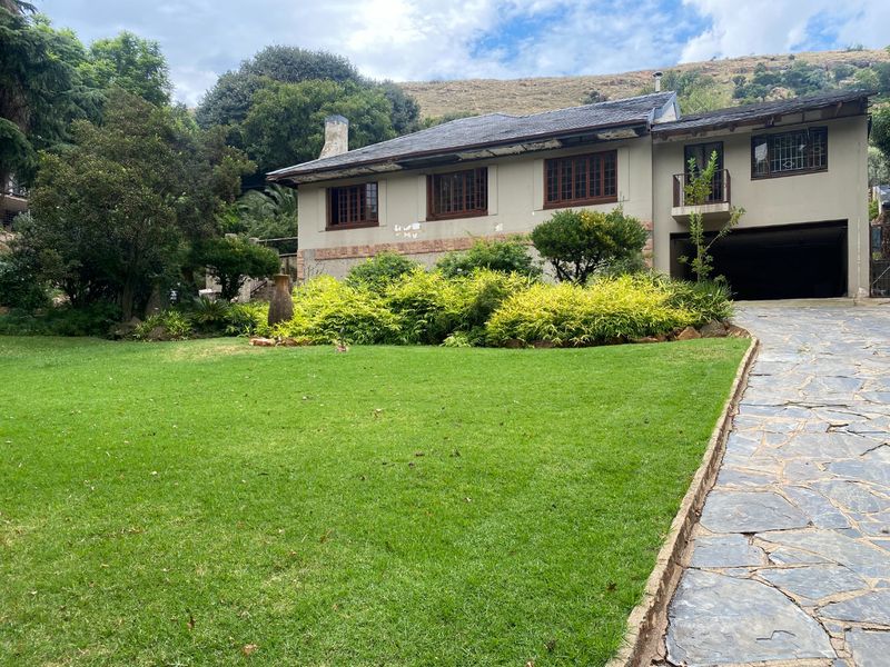 A two-story residential property featuring a stone-paved driveway, landscaped front garden, and integrated garage, set against a natural hillside backdrop.