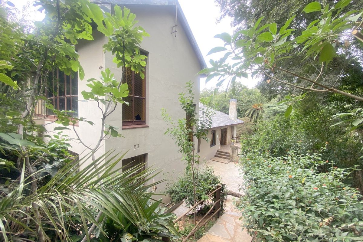 A view of the rear exterior elevation of the house, featuring stone pathways, mature garden landscaping, and a multi-level building structure.