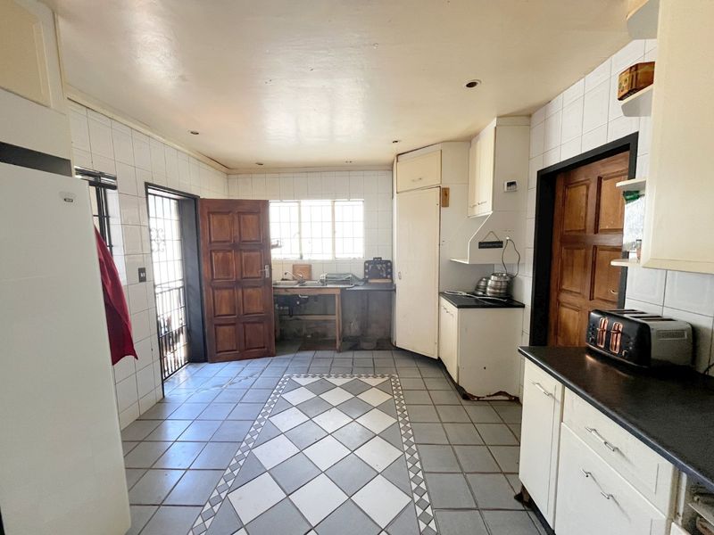 A dated kitchen featuring tiled flooring, basic cabinetry, and a functional layout with direct access to an exterior door.
