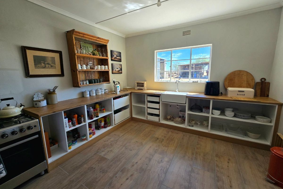 A rustic-style kitchen featuring open shelving, wooden countertops, a farmhouse sink, and a freestanding stove with wood-look laminate flooring.