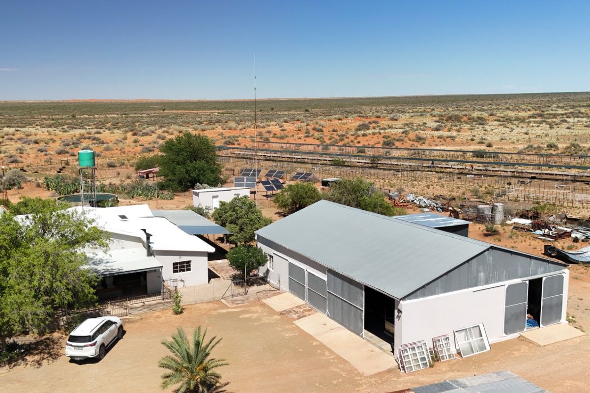 Aerial view of a farm property featuring a main dwelling, large workshop shed, solar panel array, and water storage tank in a rural landscape.