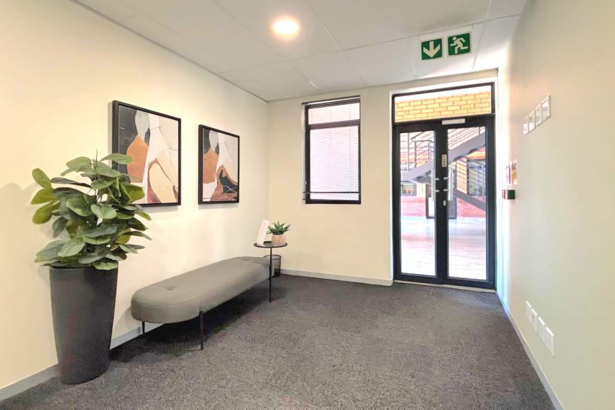 A clean and professional commercial entrance lobby featuring carpeted flooring, recessed lighting, and a secure aluminium-framed glass door leading to the exterior.