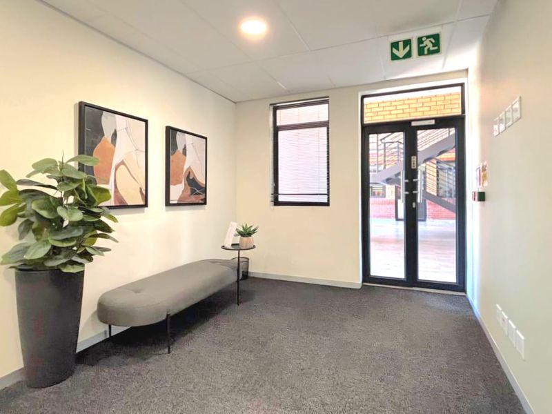 A clean and professional commercial entrance lobby featuring carpeted flooring, recessed lighting, and a secure aluminium-framed glass door leading to the exterior.