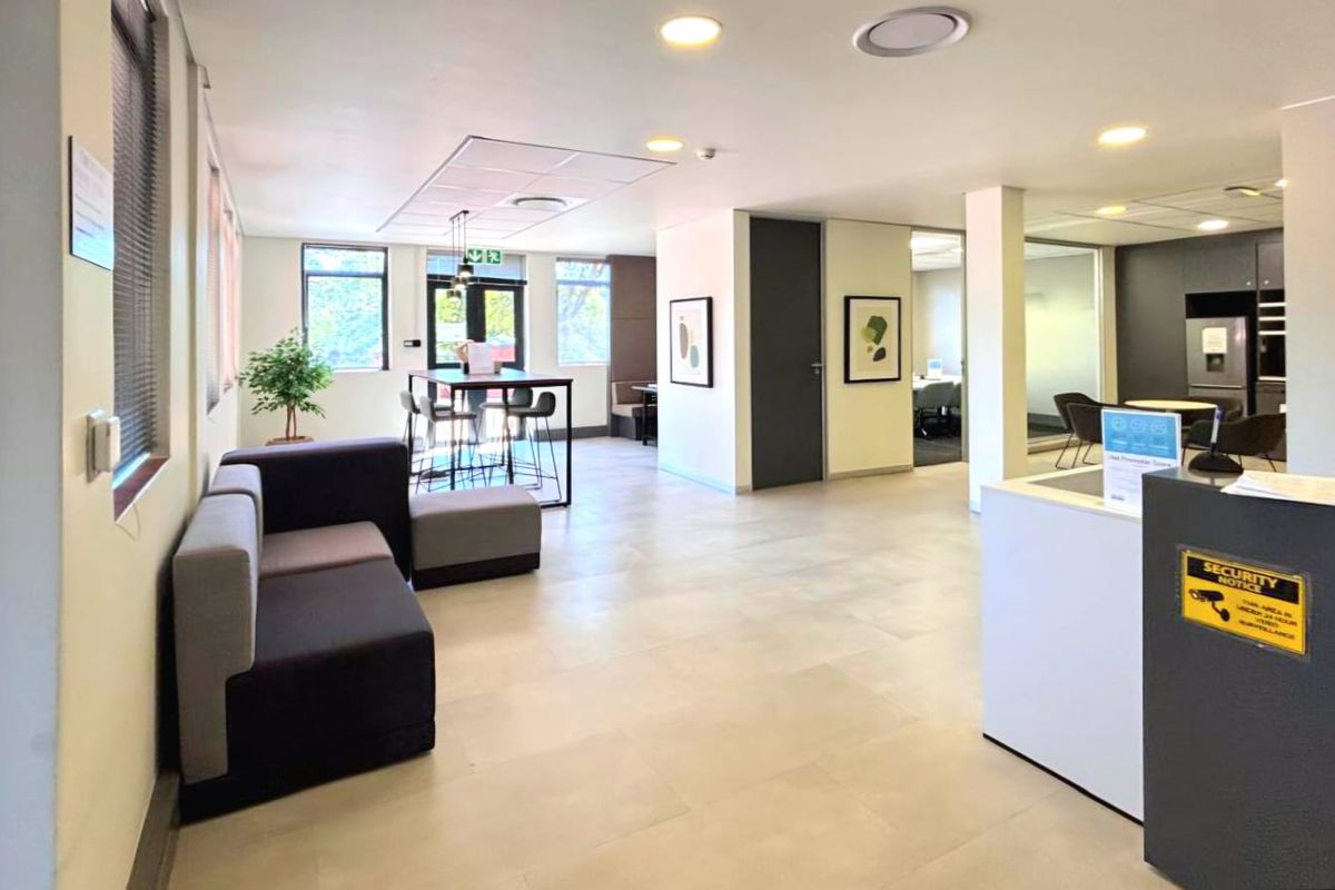 Modern open-plan commercial office space featuring a reception area, tiled flooring, recessed lighting, and glass-partitioned meeting rooms.