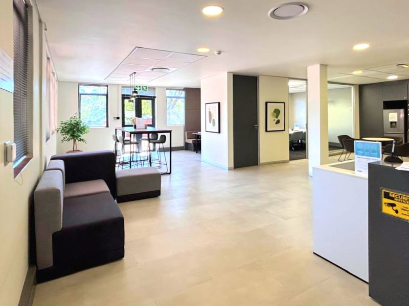 Modern open-plan commercial office space featuring a reception area, tiled flooring, recessed lighting, and glass-partitioned meeting rooms.