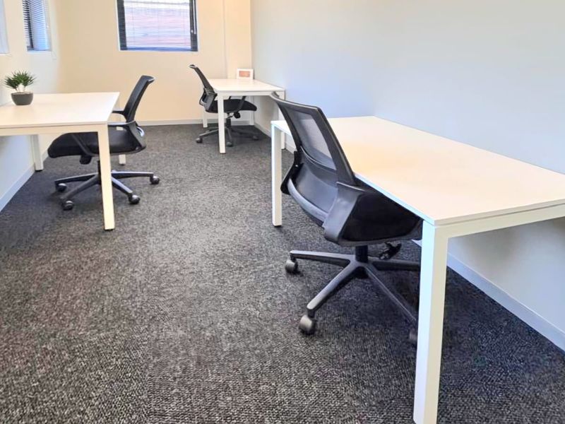 A clean, professional office space featuring neutral walls, carpeted flooring, and natural light provided by multiple windows with fitted blinds.