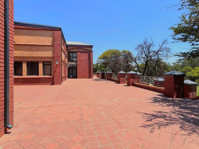 Spacious outdoor brick-paved patio area featuring brick pillars, metal railings, and views of the surrounding landscape.