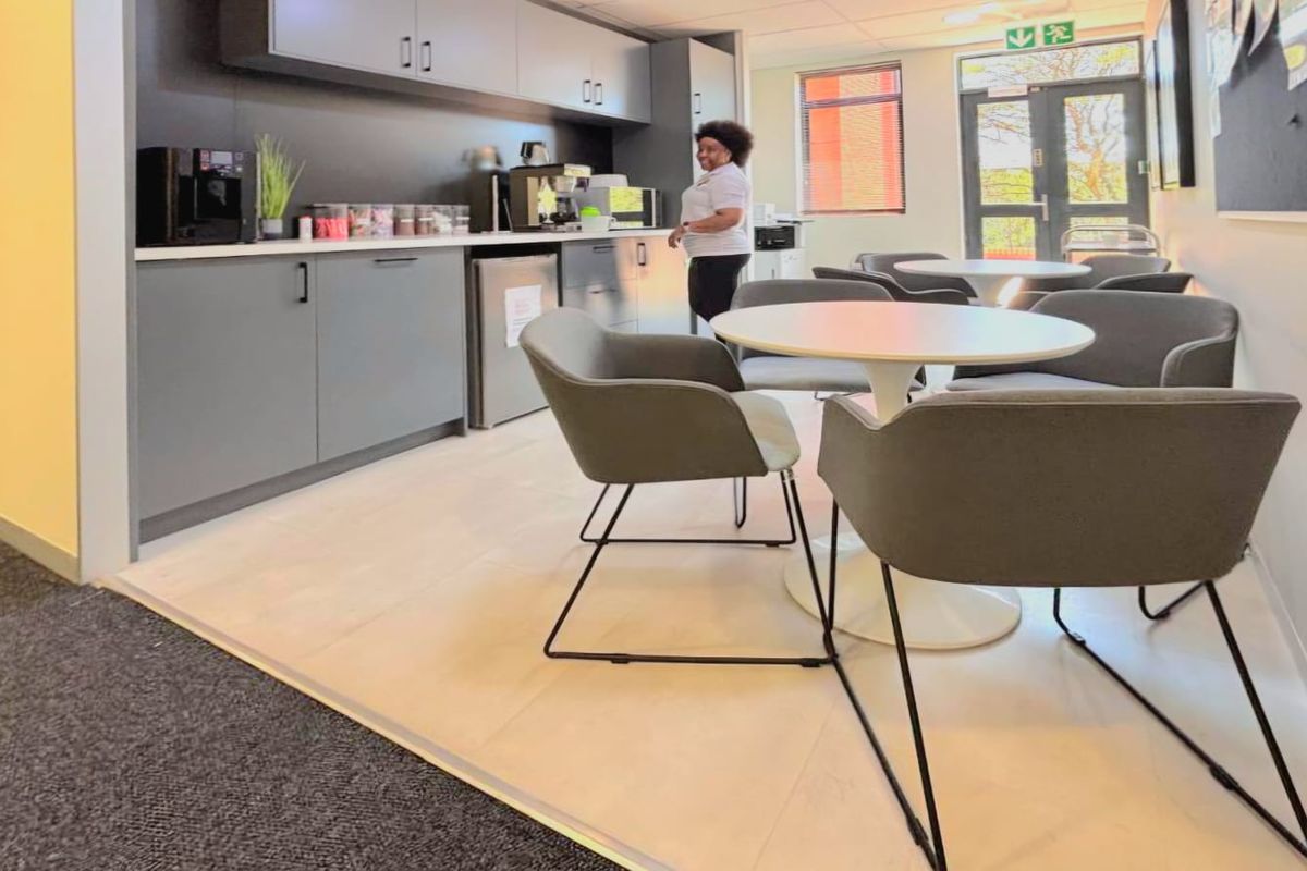 A modern office kitchenette featuring sleek grey cabinetry, light wood-look flooring, and direct access to an outdoor area through a glass door.