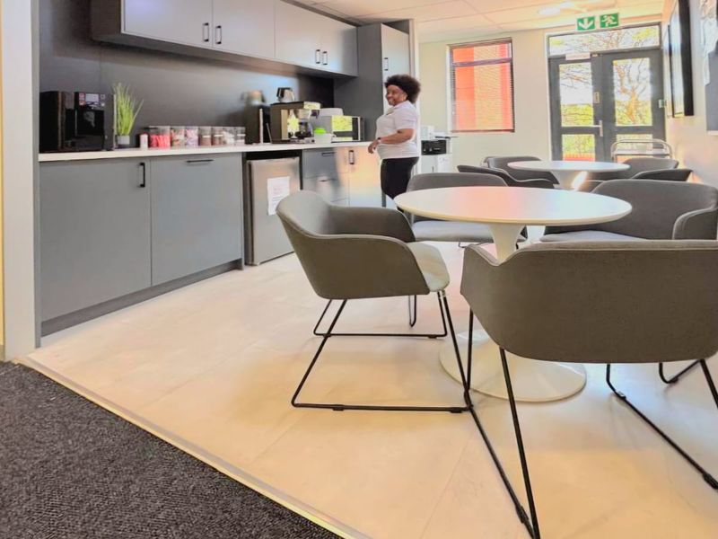A modern office kitchenette featuring sleek grey cabinetry, light wood-look flooring, and direct access to an outdoor area through a glass door.