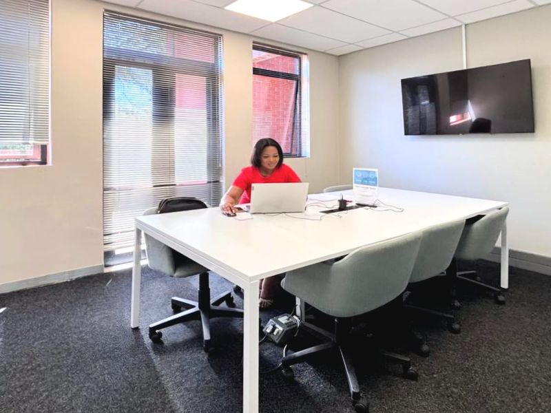 A functional commercial office space featuring carpeted flooring, suspended ceiling tiles, and large windows with venetian blinds, suitable for professional meetings.