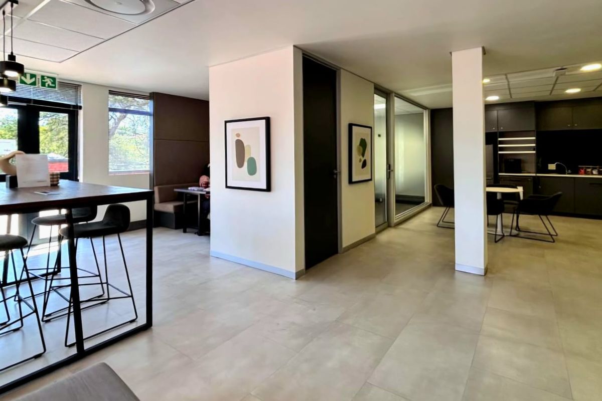 Modern open-plan commercial office space featuring tiled flooring, recessed lighting, glass partitions, and a sleek integrated kitchenette area.