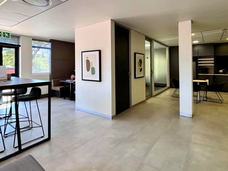 Modern open-plan commercial office space featuring tiled flooring, recessed lighting, glass partitions, and a sleek integrated kitchenette area.