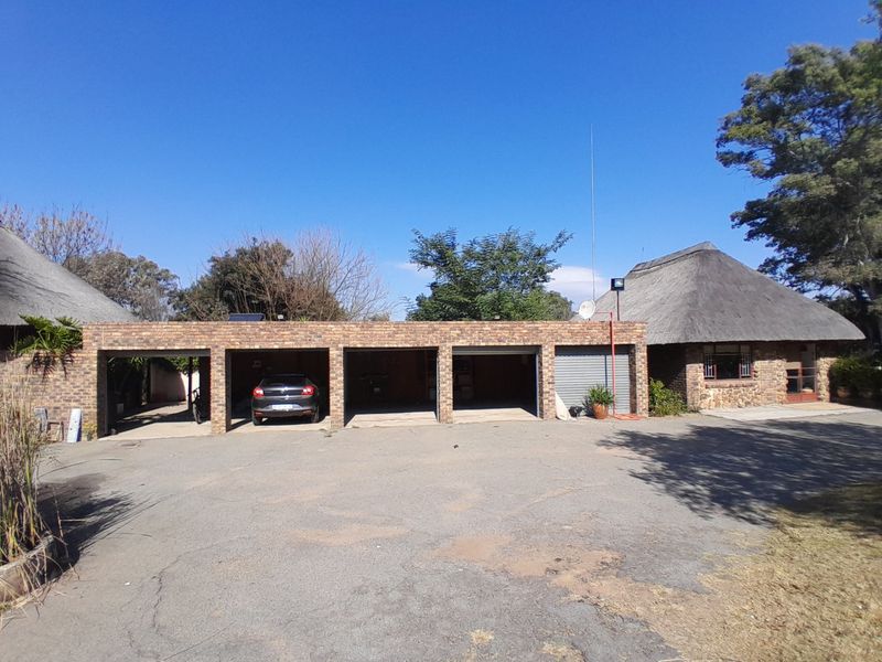 Front view of the property featuring a multi-bay brick garage structure and a traditional thatched roof, set against a large asphalt driveway.
