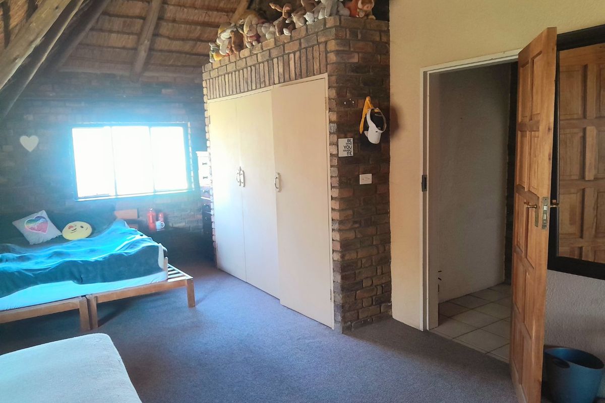 Bedroom featuring an exposed thatch ceiling, brick feature wall, and built-in storage, offering a rustic aesthetic with potential for modern updates.
