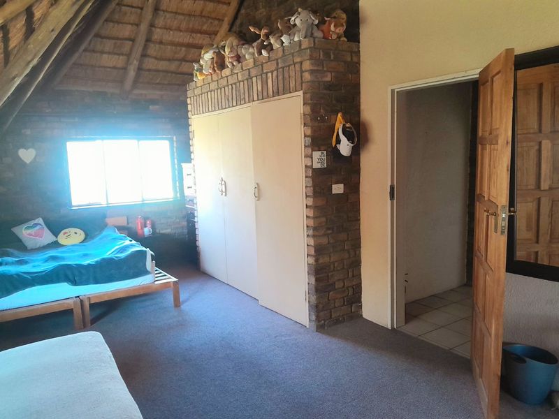 Bedroom featuring an exposed thatch ceiling, brick feature wall, and built-in storage, offering a rustic aesthetic with potential for modern updates.