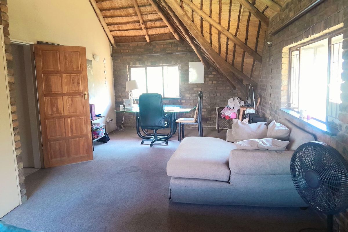 A rustic living area featuring exposed brick walls, a high thatched ceiling with timber rafters, and natural light from multiple windows.