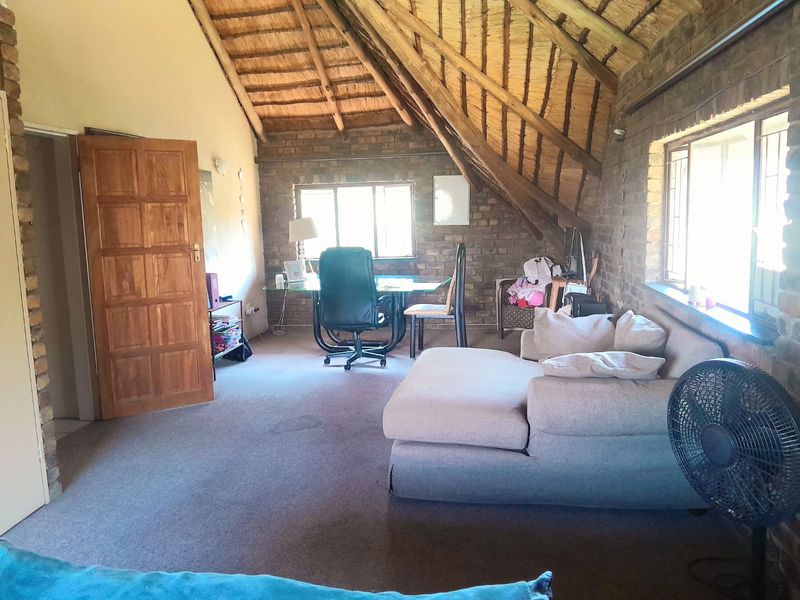 A rustic living area featuring exposed brick walls, a high thatched ceiling with timber rafters, and natural light from multiple windows.